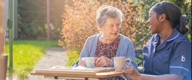 Elderly outside with a carer having a cup of tea