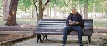 Elderly man sitting in a park alone reading a book