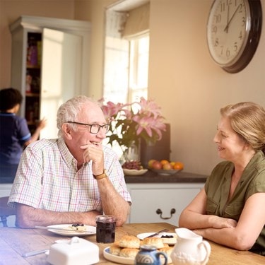 Father & daughter laughing in kitchen with scones and a Bluebird Care worker in the background.