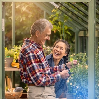 A man and woman smile joyfully together inside a vibrant greenhouse filled with lush plants.