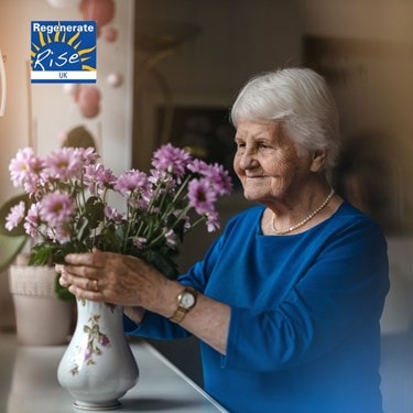 elderly lady alone putting a vase with flowers on the table