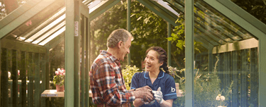 Professional caregiver assisting an older man with gardening activities.