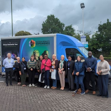 Virtual dementia experience truck with people standing in front of it for a photo