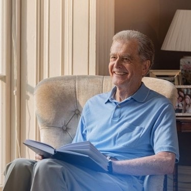Elderly man sitting on a couch at home reading a book