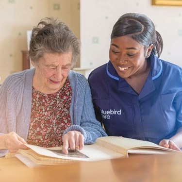 A carer and an elderly lady looking at  photo album