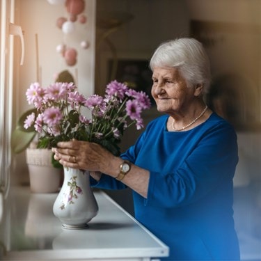 An older woman gently holds a vase filled with vibrant flowers.