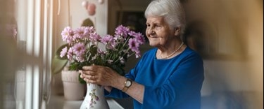 An older woman holds a vase filled with vibrant flowers.