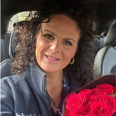 Wendy pictured in Bluebird Care uniform holding a bunch of red roses