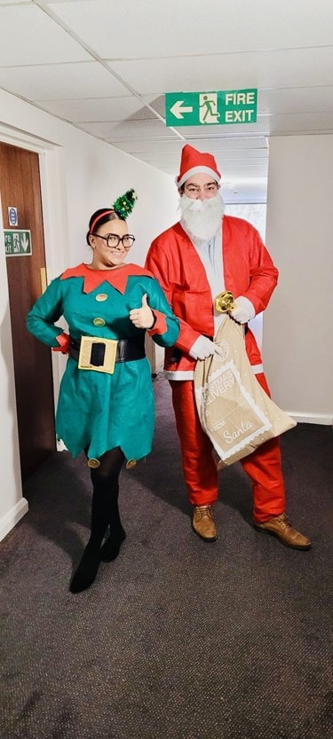 Sinead & Julian dressed as Santa and an elf delivering Christmas gifts