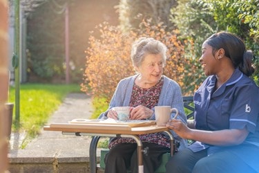 A Bluebird Care Care Expert sharing a cup of tea with an older lady in an autumn garden