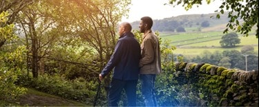 a walk in the countryside with a family member assisting his dad who has a walking stick
