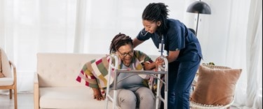 Carer assisting a lady to get off the couch with her walker