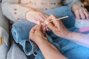 A close-up of a carer gently providing nail care for an older person at home.