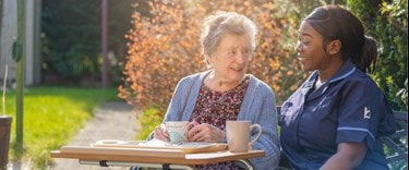 Elderly lady outside chatting and having tea with a carer