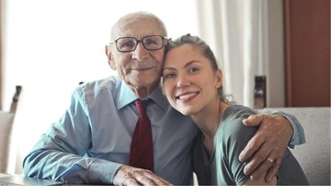 Elderly man and young woman smiling warmly while embracing in a close, affectionate pose.