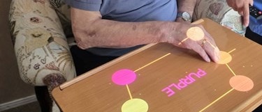 Older man using an interactive Happiness Programme activity projected onto his table at home