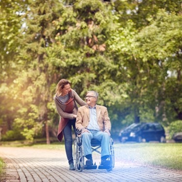 A woman assists an elderly man by pushing him in a wheelchair.