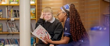 Carer reading with a child in a school library, supporting learning and confidence through care