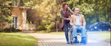 Lady pchatting and ushing an elderly man in a wheelchair outside