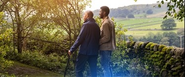 a walk in the countryside with a family member assisting his dad who has a walking stick