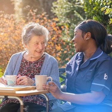 Elderly lady chatting with her carer outside over a cup of tea