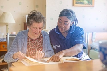 A Bluebird Care Care Expert sharing a book with a customer at the kitchen table