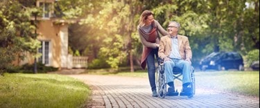 A woman assists an elderly man by pushing him in a wheelchair