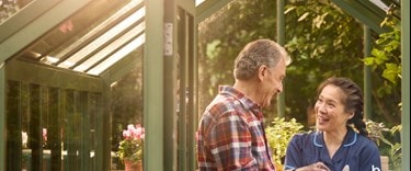 Elderly man and care assistant chatting in a greenhouse