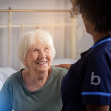 A nurse smiles warmly at an elderly woman resting in bed