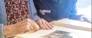 elderly lady looking at a picture in a book with a carer