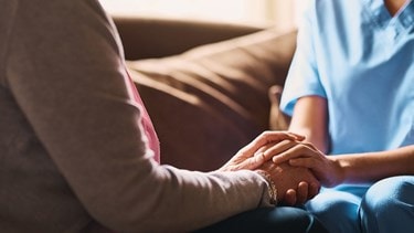 Caregiver in blue scrubs holding the hands of an elderly person, offering comfort and support