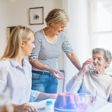 family at the kitchen table with elderly lady drinking water