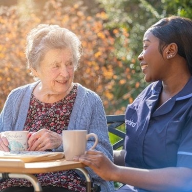 A carer and an elderly sitting outside having a cup of tea