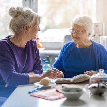Elderly Lady and a family member chatting at the table with an open book 
