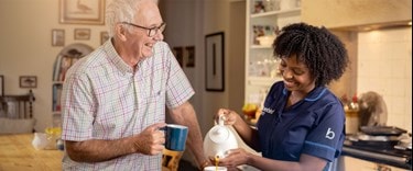 Smiling caregiver pouring tea for an elderly man in a cozy kitchen setting