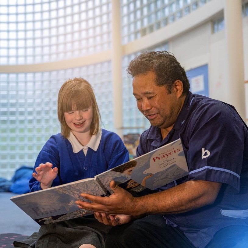 Bluebird Care Care Expert helping a pupil read a book.
