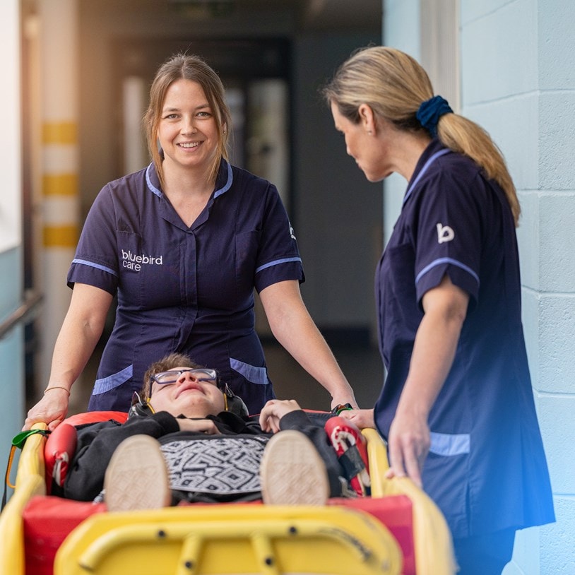 Bluebird Care Assistants moving a customer using a patient transfer trolley