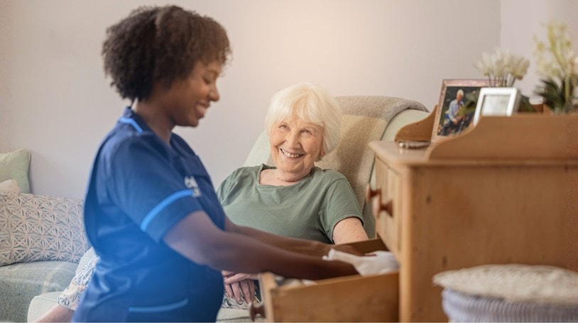 Carer putting away clothes in the drawer for an elderly lady