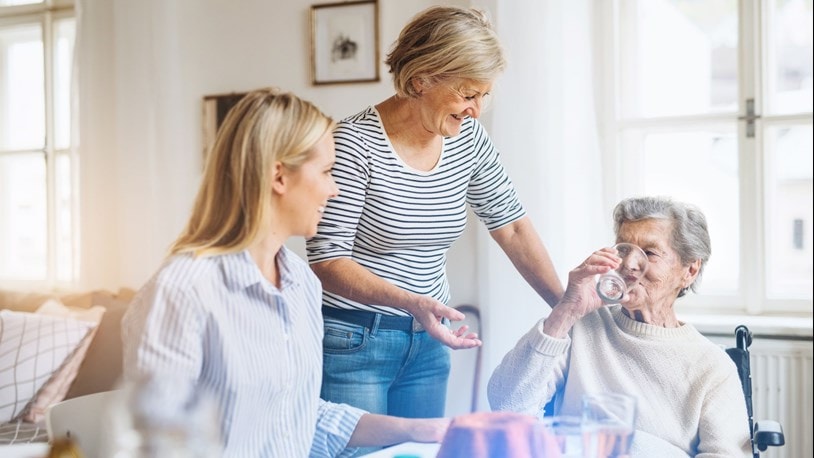 family at the kitchen table with elderly lady drinking water